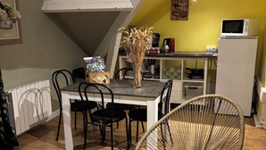 A dining area with a table, chairs, a vase of dried plants, and a kitchen in the background.