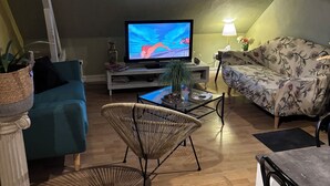 A cozy living room with a television, a sofa, a chair, and a table with a lamp.