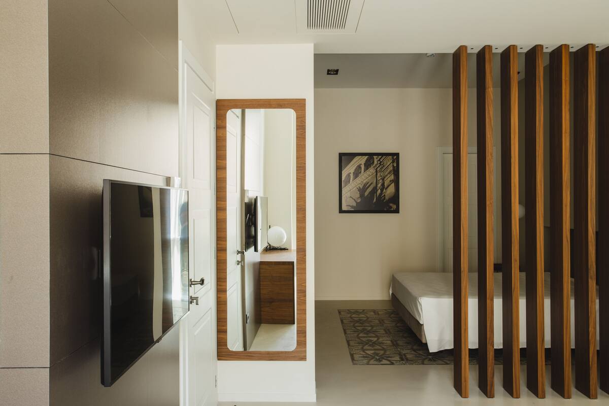 A compact hotel room with a bed, a mirror, a wardrobe, and a television.