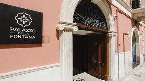 The entrance to Palazzo della Fontana with a black signboard, an arched doorway, and a wooden door. - Palazzo della Fontana (Matera)