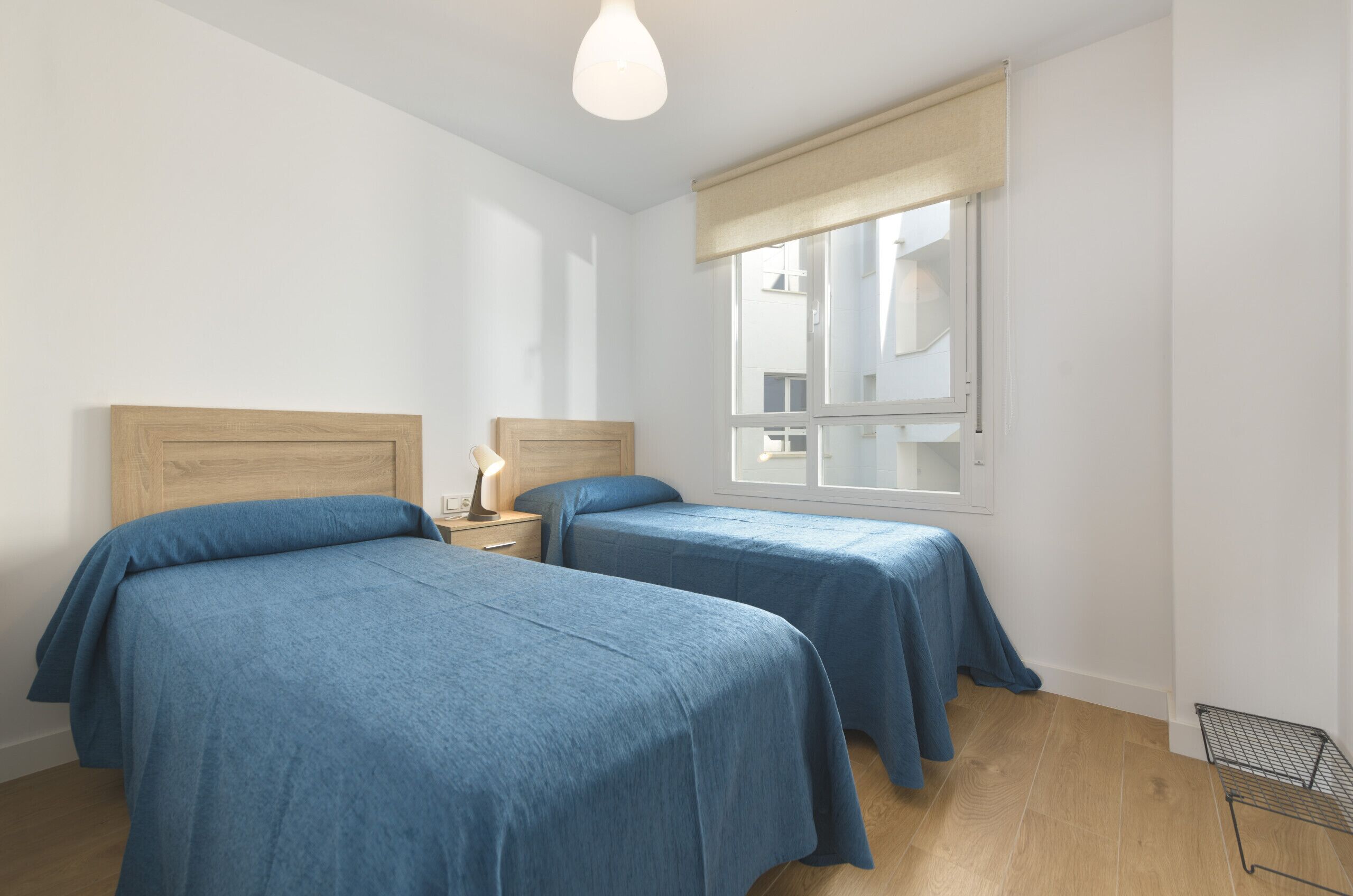 Una camera da letto con due letti, un comodino con una lampada, una finestra con vista e una rastrelliera in metallo.