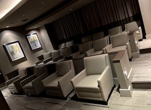 Relax in a cinema room with plush seats and a minimalist design, featuring a large screen and framed artworks on the walls.