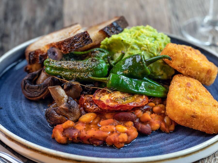 Een bord eten met diverse ingrediënten, zoals bonen, champignons en een stuk brood.