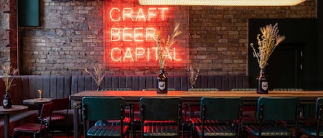 A bar area with a neon sign reading "CRAFT BEER CAPITAL," wooden bar stools, and a brick wall.