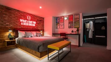 Un dormitorio moderno con pared de ladrillo, un letrero de neón, una cama, un banco, un escritorio y un vestidor.