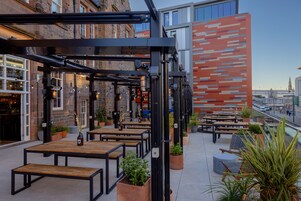 An outdoor seating area with tables and chairs, potted plants, and a modern building facade in the background.