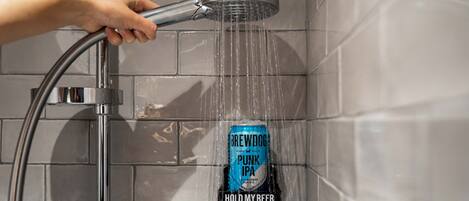 Una mano sostiene un cabezal de ducha con agua fluyendo sobre una lata de cerveza BrewDog Punk IPA, con la etiqueta que dice 'HOLD MY BEER'.