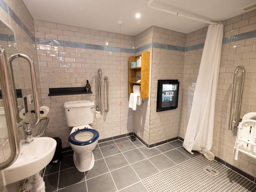 A bathroom with a toilet, sink, shower, and a handrail.