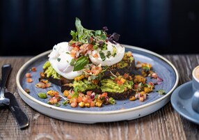 A plate of food with avocado toast topped with poached eggs and a variety of fresh toppings.