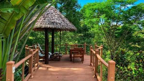 A wooden deck with a thatched-roof gazebo, surrounded by lush greenery.