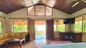 A spacious room with a large bed, a sofa, and a television. There are large windows and a balcony.