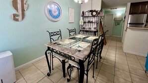 Un coin repas avec une table dressée pour quatre personnes, entourée de chaises. Un mur est orné d’une horloge et d’une assiette décorative au-dessus de la table.