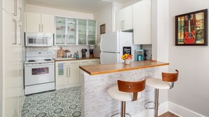 Una cocina moderna con armarios blancos, microondas, estufa, refrigerador y una barra con dos taburetes.