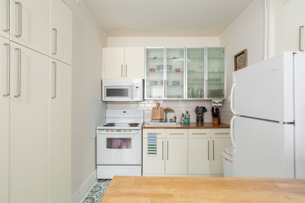 A compact kitchen with white cabinets, a microwave, stove, and refrigerator. - Near Belmont & VUMC · 1BR Sleeps 4 · 1920s Condo (Nashville)
