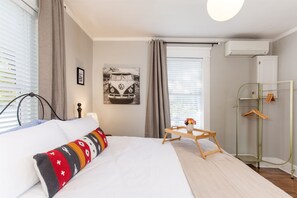 A neatly arranged bedroom with a bed, a bedside table with a tray, a hanging clothes rack, and a window with blinds. - Near Belmont & VUMC · 1BR Sleeps 4 · 1920s Condo (Nashville)