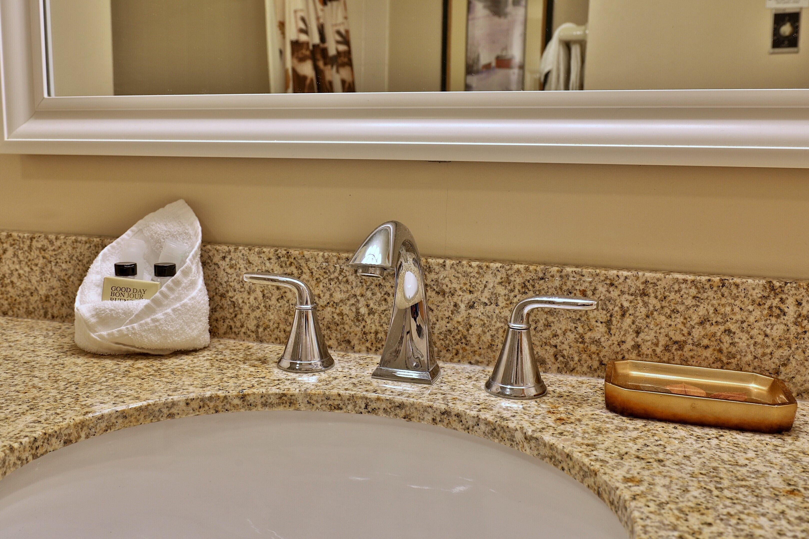 Un lavabo de salle de bain avec un plan de travail en granit, une serviette, un porte-savon et un miroir au-dessus.