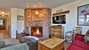 A cozy living room with a brick fireplace, a television, and a red couch. - How to Lose Your Ski Pass in 10 Days with Mountain Views on Shuttle Route A1 (Killington)