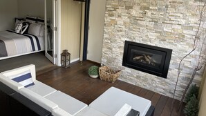 Ein modernes Wohnzimmer mit Steinwand, Kamin, einem Bett mit gestreifter Bettwäsche und einem Korbsessel.