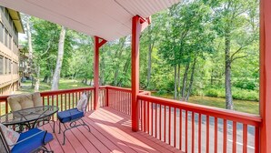 A covered outdoor deck with red railings, a table with blue chairs, and a view of a forested area.