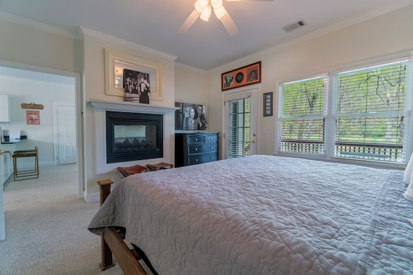 A bedroom with a fireplace, a large bed, a desk, and a window with blinds.