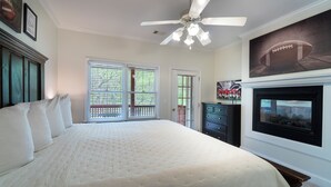 Un dormitorio con una cama grande, un ventilador de techo, una chimenea y vistas al exterior a través de las ventanas.
