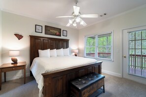 Une chambre à coucher avec un grand lit, une tête de lit en bois, un banc, deux tables de chevet et un ventilateur de plafond.