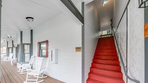 Un espacio al aire libre cubierto con sillas mecedoras blancas, una escalera roja y un letrero de precaución.