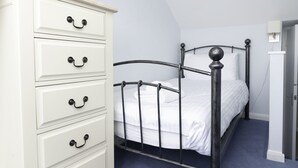 Un dormitorio con un tocador blanco, estructura de cama metálica y alfombra azul.