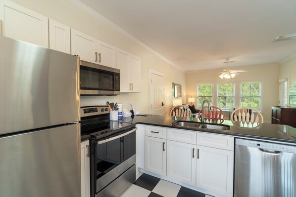 A modern kitchen with stainless steel appliances, white cabinetry, and a black and white checkered floor. - #502 Victory Lane Suite| 1 BR| Helen| on River (Helen)
