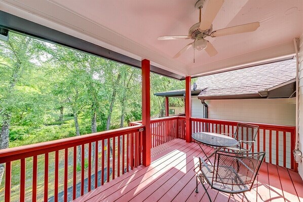 A covered porch with a table and chairs, a ceiling fan, and a view of trees.