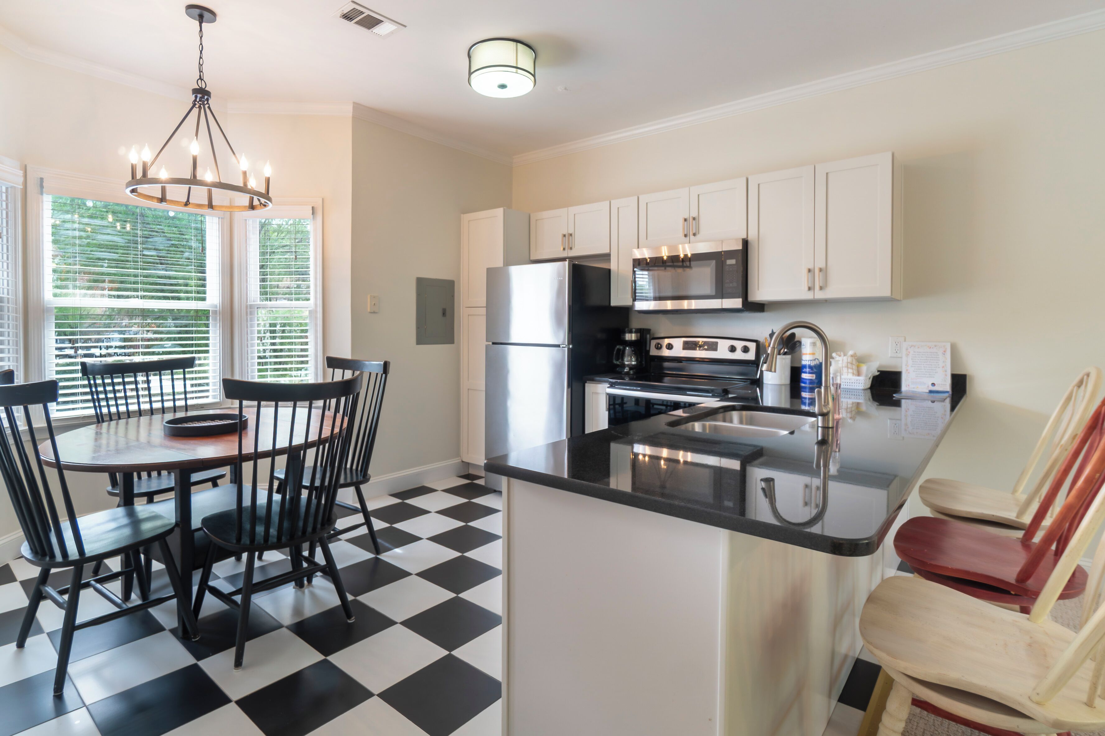 A kitchen with a black and white checkered floor, a dining table with chairs, a refrigerator, a microwave, and a sink.