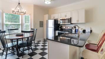 A kitchen with a black and white checkered floor, a dining table with chairs, a refrigerator, a microwave, and a sink.