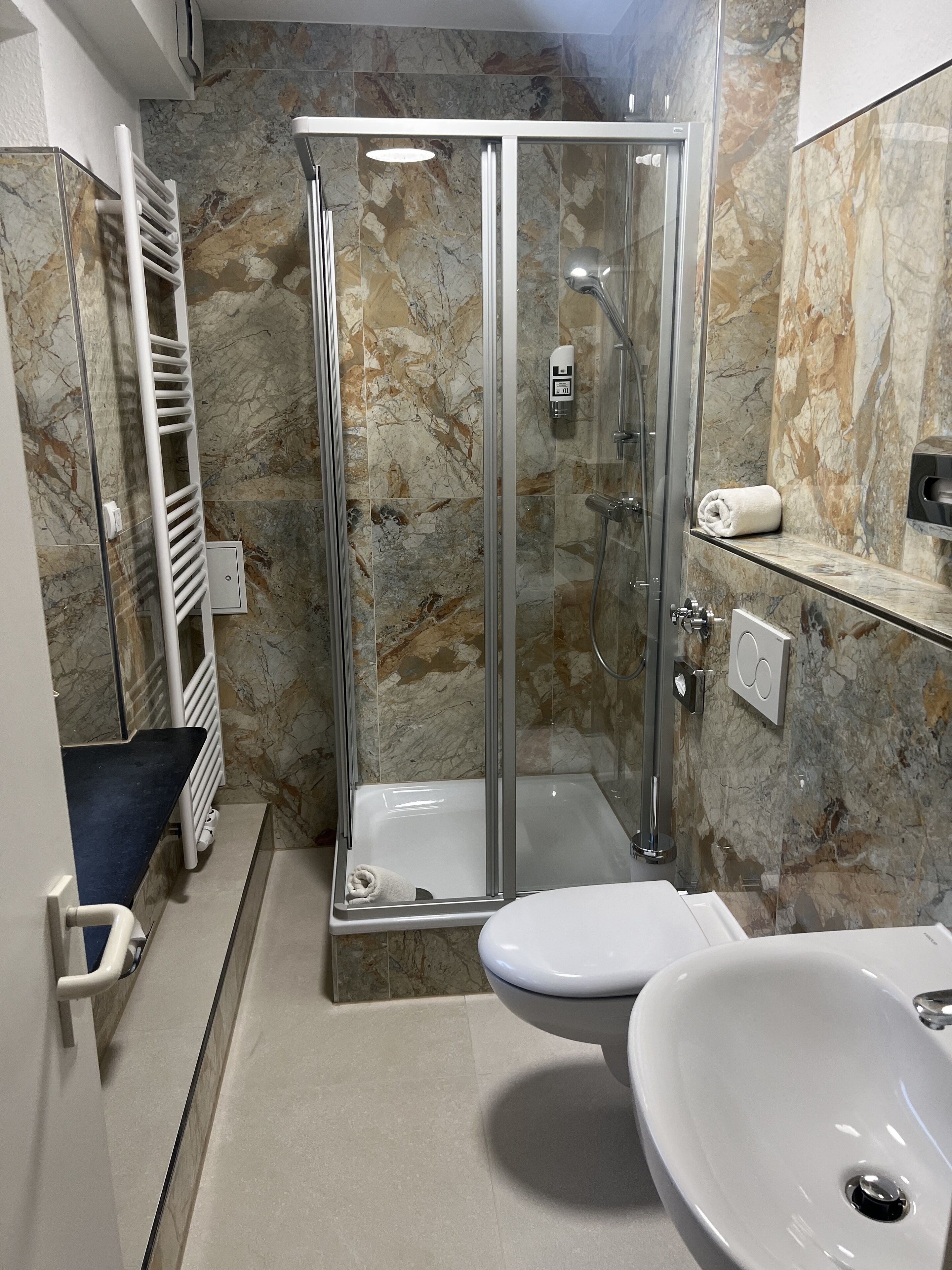A modern bathroom with a glass-enclosed shower, a white sink, and marble walls.