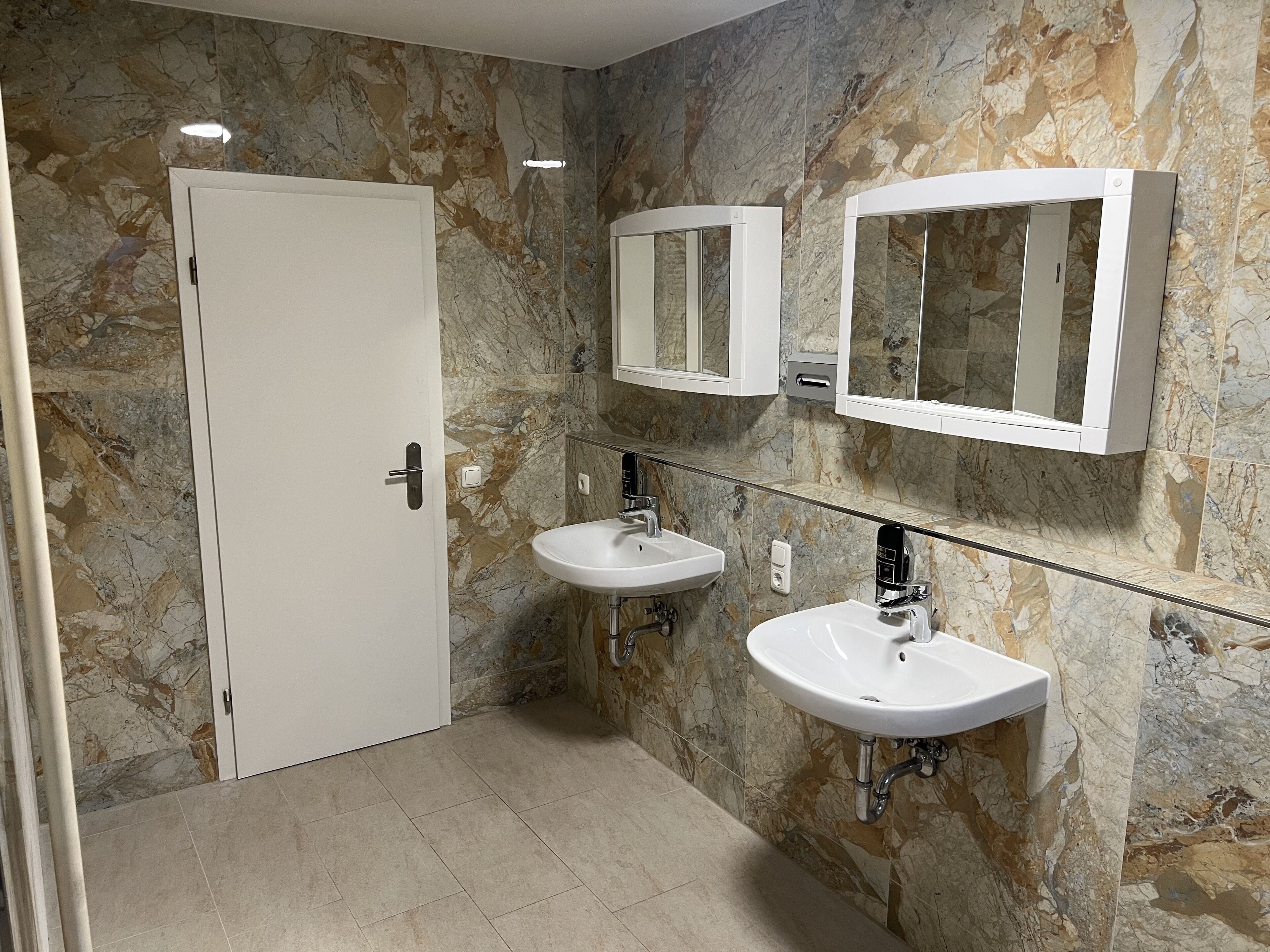 A bathroom with two sinks, a door, and marble walls.