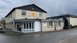 Ein zweistöckiges Gebäude mit Schildern für 'M&M Hotels' und 'Derboven', welche ein Hotel und Restaurant kennzeichnen.