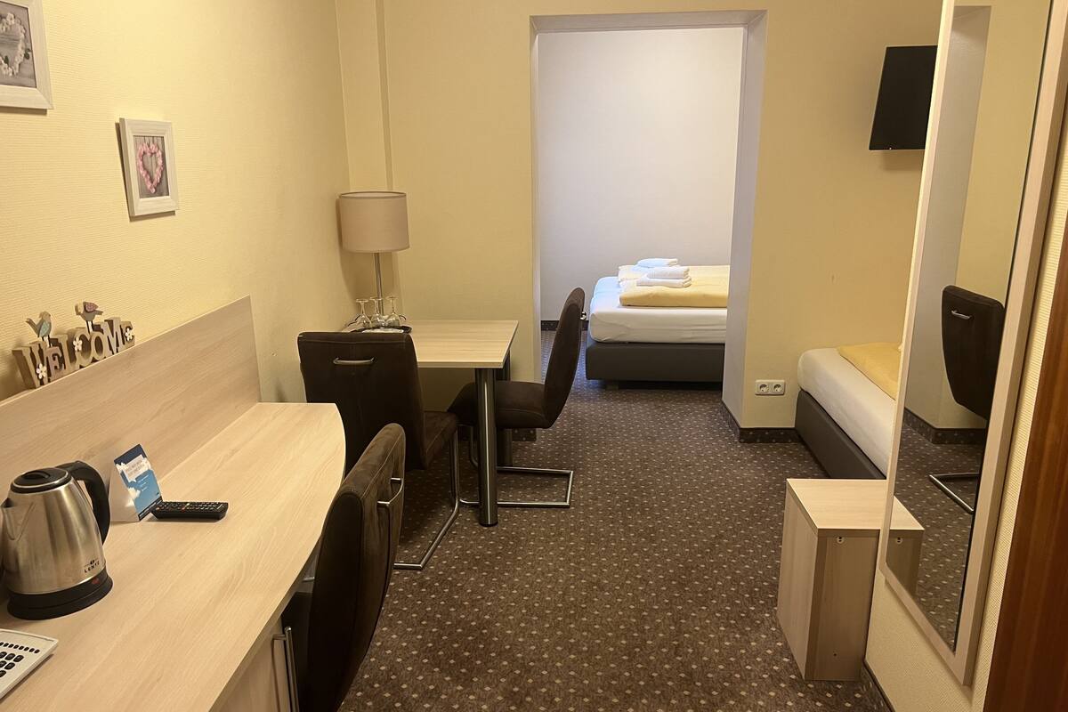 Une chambre d’hôtel comprenant un lit, un bureau avec une lampe, une chaise, une machine à café et une petite table avec un porte-cartes.