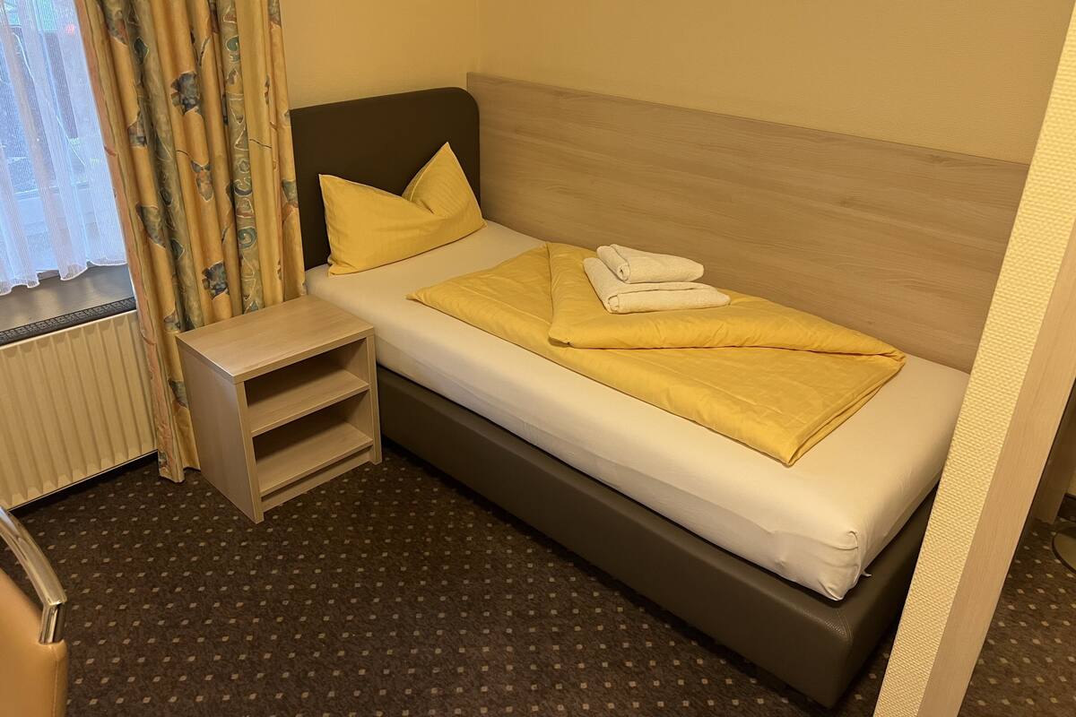 Un lit simple avec une tête de lit en bois, une table de chevet et une petite étagère.