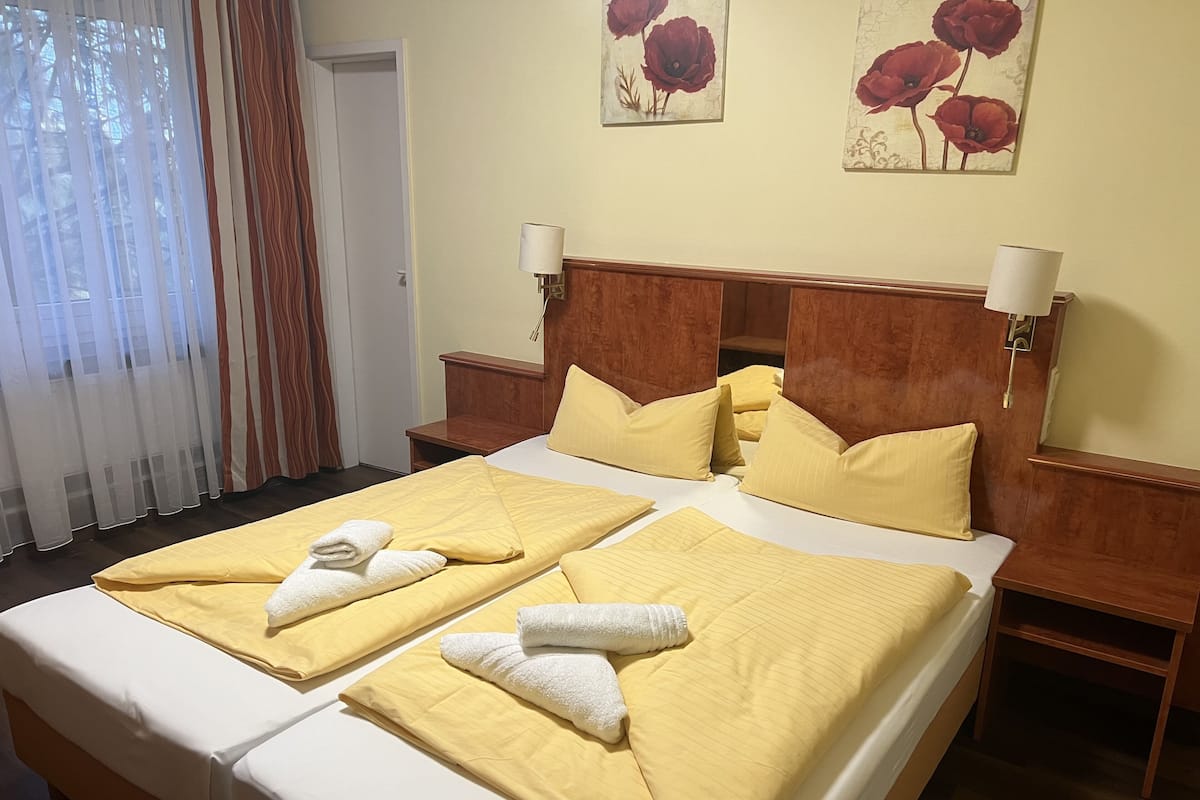 Un lit double avec une literie et des serviettes de couleur jaune, une tête de lit en bois, des lampes de chevet et une décoration florale au mur.