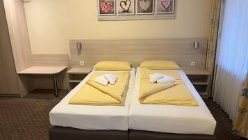A hotel room with two beds, a small desk, and a wall-mounted picture frame with heart-shaped decorations.