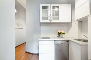 Una cocina compacta con muebles blancos, un lavavajillas y un lavabo.