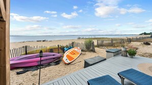 Une vue sur la plage avec une terrasse en bois, des kayaks et une planche de paddle.