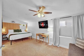 A hotel room with a bed, desk, chair, ceiling fan, TV, and window with curtains. - Beachfront Sunsets on the Water at Oakwood Beach (Salem)