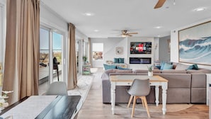 Un salon moderne avec un canapé, une table à manger et des chaises. On y trouve un ventilateur de plafond et une grande fenêtre avec des rideaux.