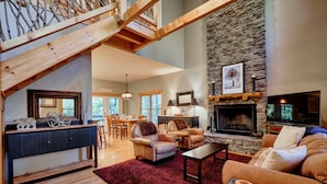 A spacious living area with a stone fireplace, leather sofas, and a wooden staircase.