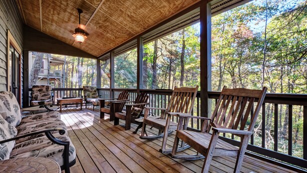 A wooden deck with rocking chairs and a bench, overlooking a forested area.
