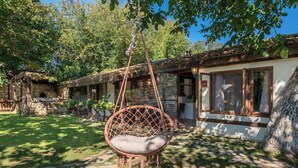 A rustic outdoor seating area with a hanging chair, a stone pathway, and a building with large windows and a tiled roof. - Villa Viara in Rural Pchelnik (Pchelnik)