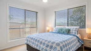 A bedroom with a bed, two bedside tables, and a window with blinds. - The Weekender - 4-46 Cypress Street (Evans Head)