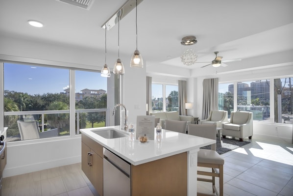 Una cocina moderna con una isla grande, un área de comedor con sofá y sillas, y ventanas amplias con vistas a la ciudad.