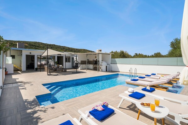 Área de piscina no terraço com espreguiçadeiras, mesa de jantar e cozinha.