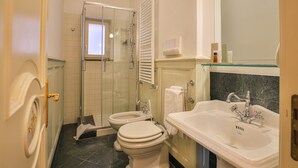 Un baño con ducha de vidrio, dos inodoros, un lavabo y un espejo.